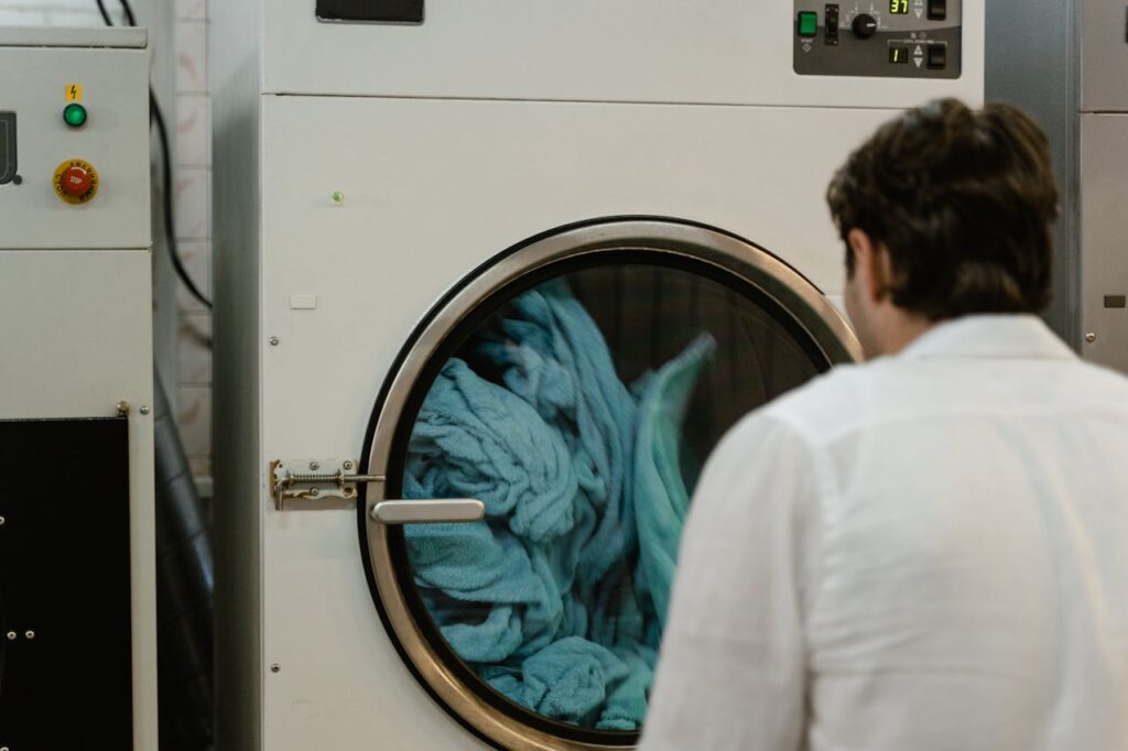 A man watches a washing machine spin in a laundromat, focusing on the process.